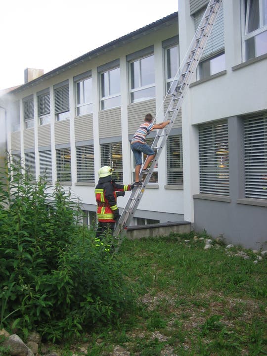 Der erste Knabe verlässt, am Seil befestigt, das Schulhaus über die Feuerwehrleiter