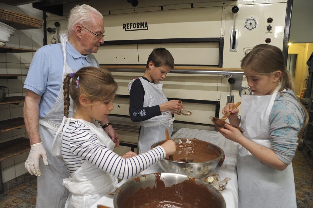Rolf Gautschi bringt die Schokolade auf die richtige Temperatur und Lukas, Ramona und Annina tragen die warme Schokomasse auf.