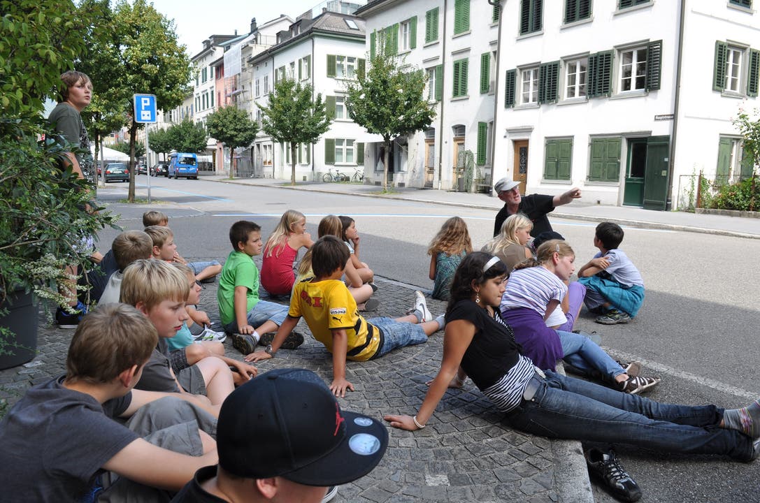 August Berlinger führt die Kinder durch Glarus Er erklärt, wie Glarus nach dem Brand mit breiten, rechtwinkligen Strassen und Häusern aus Stein und Schieferdächern neu gebaut wurde