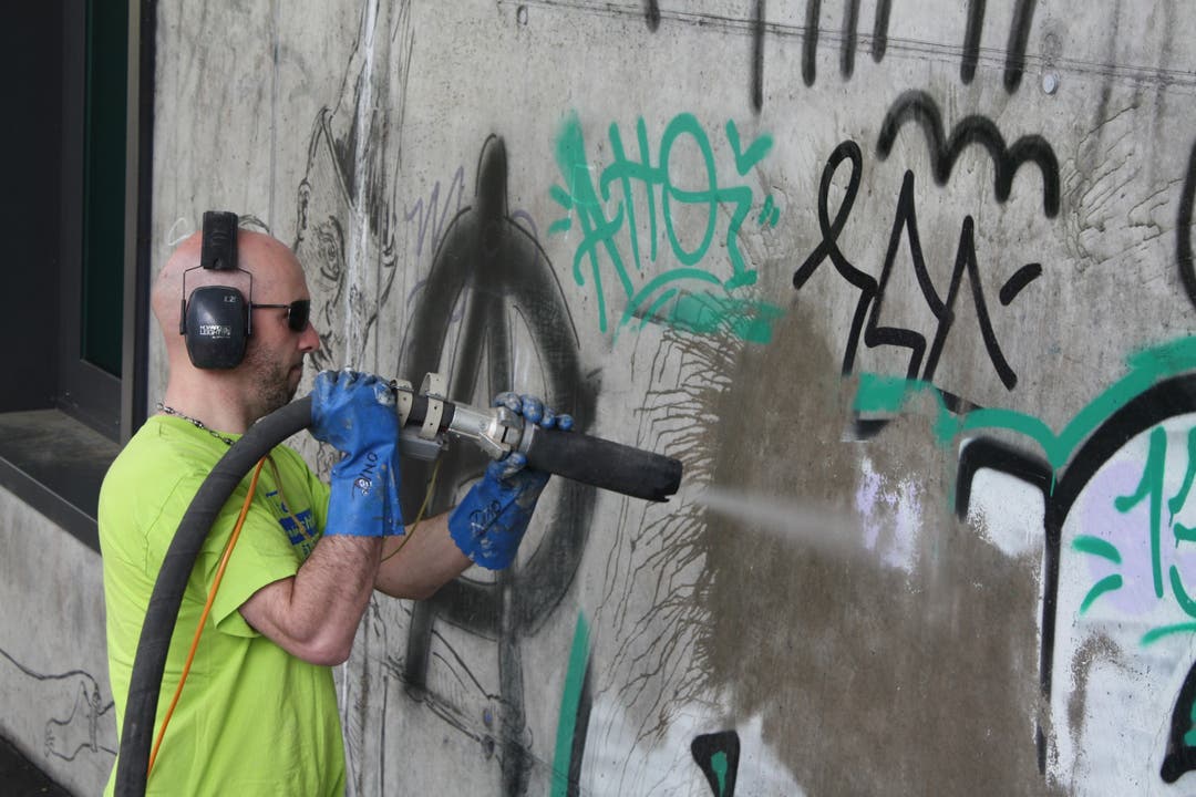 Ein Mitarbeiter der Stadtreinigung putzt mit Glaspudermehl unter Hochdruck Graffitis von den Wänden.
