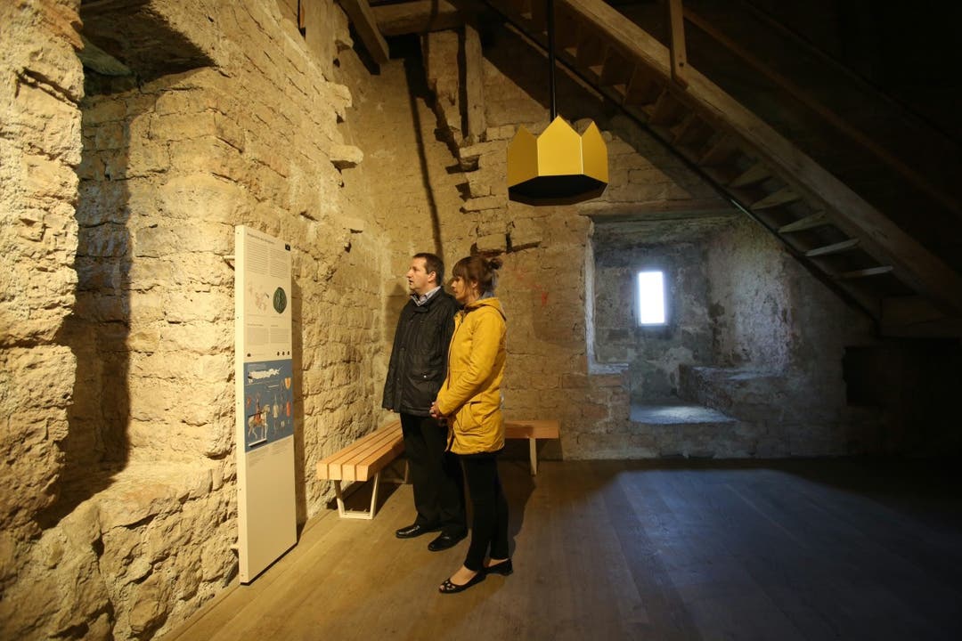 Zwei Besucher stehen an der Audiostation im Turm von Schloss Habsburg unter dem Kronensymbol