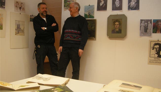 Paul Wullimann (links) stellt im Rahmen der Ausstellung, die von Otto Bitterli gestaltet wird, seine Malschule vor. Im Vordergrund Skizzenbücher, an der Wand biografische Fotos und Porträts von Amanda Tröndle.