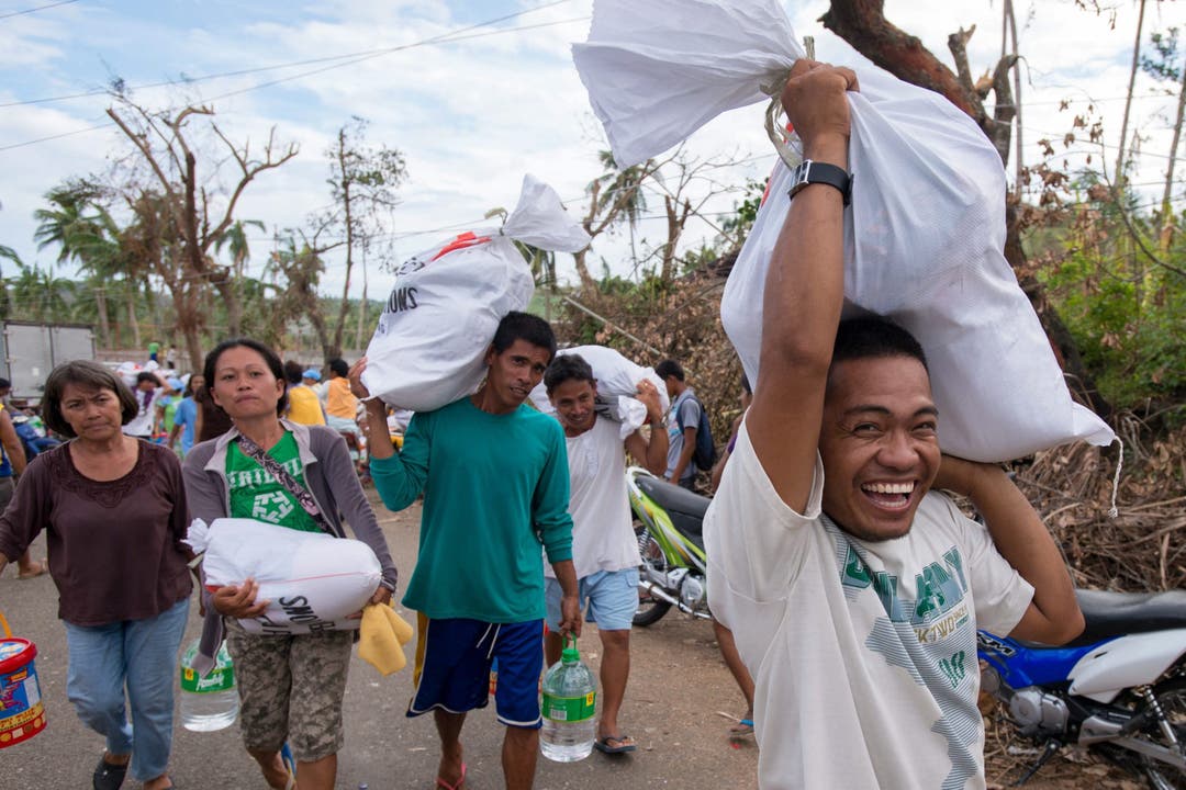 Taifun-Opfer tragen Hilfsgüter mit sich. Transportschiffe sind in Tacloban, der am schwersten getroffenen Region angekommen.