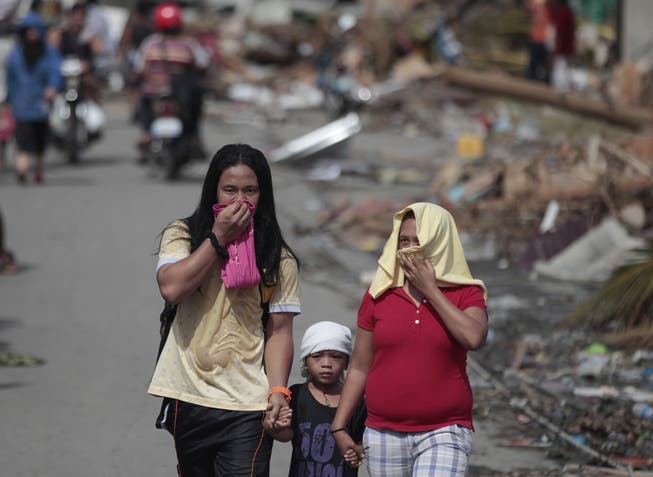 Drei Überlebende in Tacloban schützen sich vor dem Leichengestank nach dem Taifun.