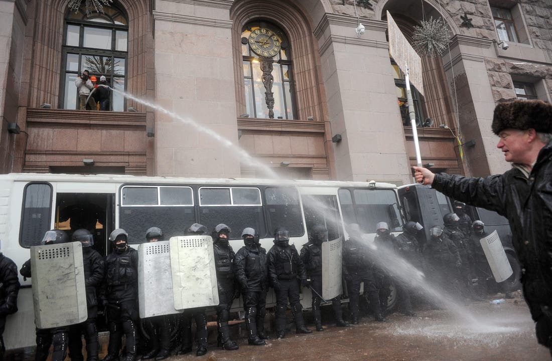 Ein Polizist spritzt mit Wasserstrahl auf Demonstranten vor dem Rathaus.