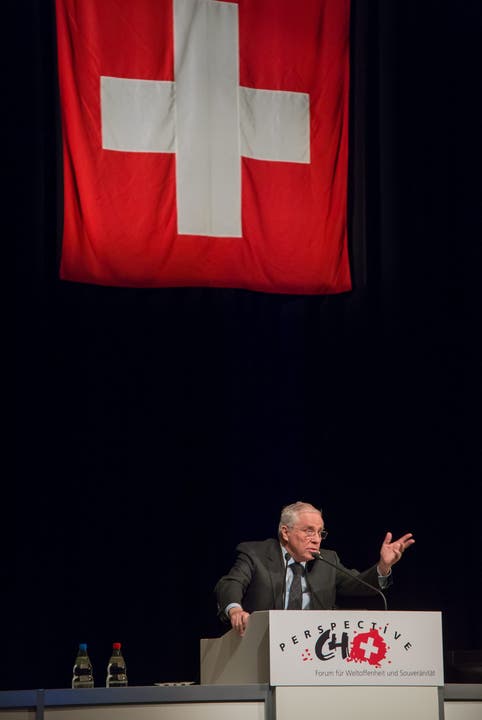 Christoph Blocher spricht, über ihm trohnt das Schweizer Kreuz.
