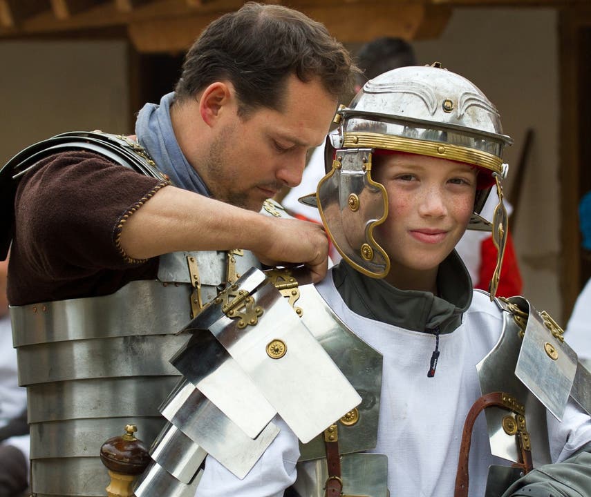 Römer entdecken auf dem Legionärspfad – ein Legionär zieht einem Jungen eine Legionärsrüstung mit Helm an