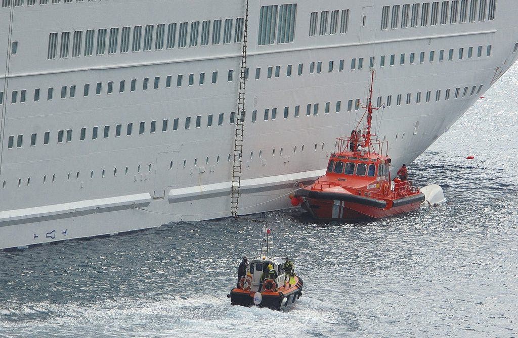 Ein Rettungschiff dockt beim Kreuzfahrtschiff an. Hiinter der Rettungsschiff ist das abgestürzte Rettungsboot zu sehen.