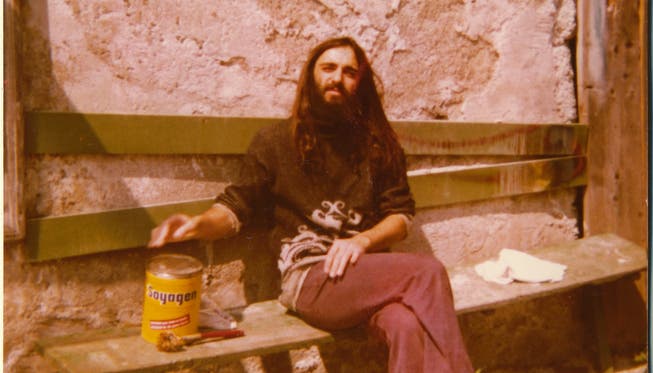 Ein ehemaliger Bewohner und Musiker mit Hippie-Frisur sitzt in der Sonne bei der berühmt-berüchtigten Kommune in Birmenstorf. zvg