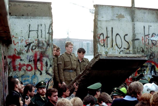 Nach 28 Jahren der Trennung begannen die Berliner nach der Grenzöffnung am 9. November 1989, die Mauer zu demontieren. Ehemalige DDR-Grenzsoldaten schauen ihnen belustigt zu.