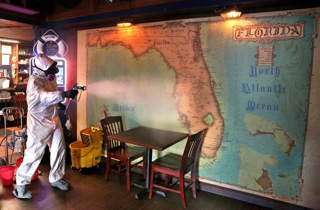 Ein Arbeiter im Schutzanzug desinfiziert die Florida-Landkarte in einem Restaurant: In den USA sind jetzt auch Staaten betroffen, die zuvor verschont blieben.