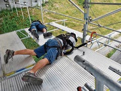 In luftiger Höhe auf schwingendem Untergrund montieren die Gerüstbauer, teils auf dem Bauch liegend, die Stahlträger und Alu-Beläge, die an den Abhängern (senkrechte Rohre) an der Energiebrücke hängen.