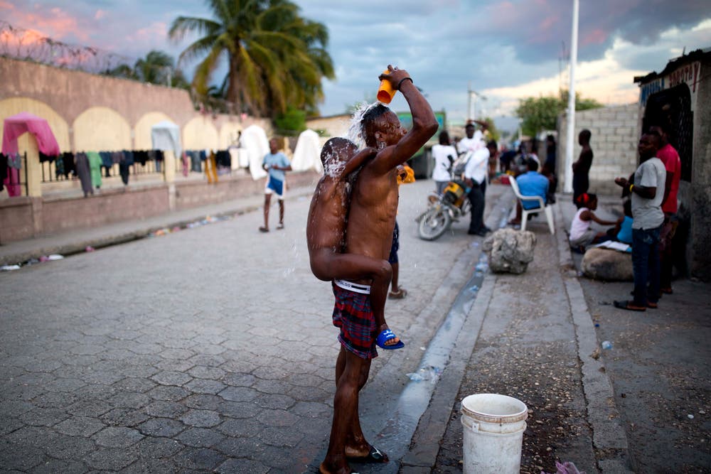 Ein Mann mit einem Kind auf dem Rücken nimmt eine Dusche in den Strassen des Slums in der Hauptstadt von Haiti. Die Behausungen der Bewohner der Slums haben meistens kein Badezimmer. (Bild: Dieu Nalio Chery/AP (Port-au-Prince, 23. November 2018))