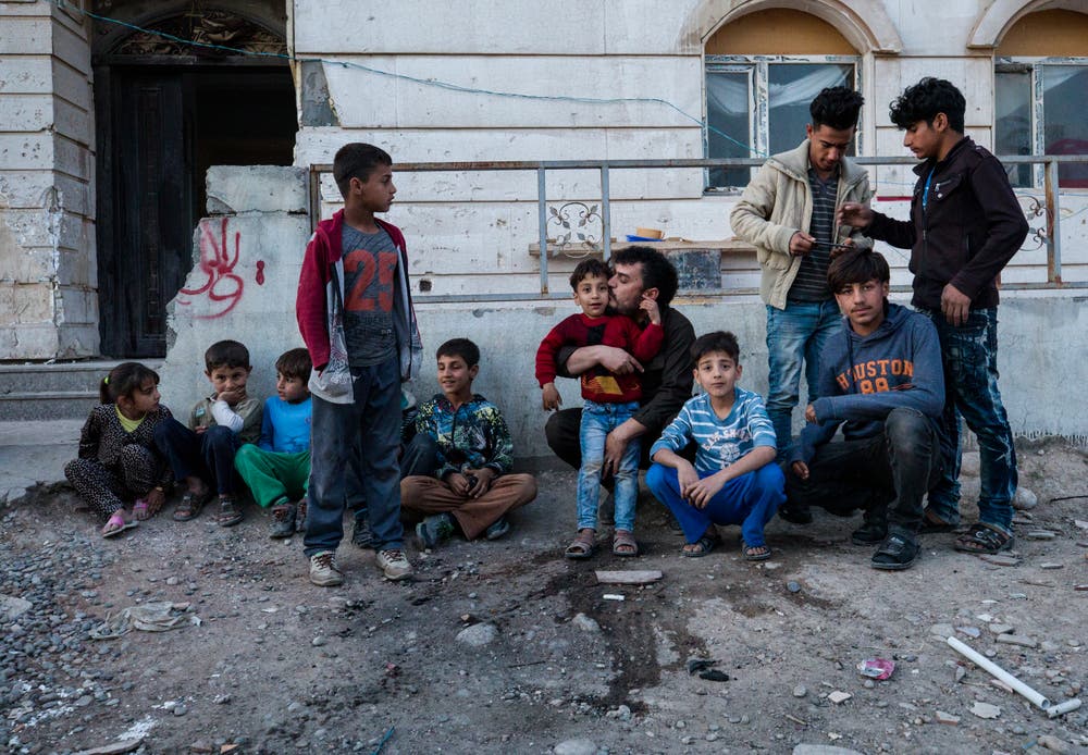 Kurdistan: Ein Mann posiert mit Kinder und Jugendlichen in einer nur im Rohbau fertiggestellten Wohnsiedlung. Die Bauruinen zeugen vom einstigen Boom und seinem Ende. Bild: Stefan Kaiser (Erbil, 17. März 2018)
