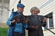 Der Kunstschaffende Ralph Brühwiler aus Ebnat-Kappel (links) überreicht Leo Morger von Kunsthalle(n) Toggenburg insgesamt 36 Postkarten mit Wünschen von den Ausstellungsbesuchern. An der Fassade im Hintergrund befand sich im September die Installation. (Bild: Anina Rütsche)