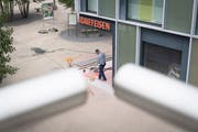 Ein Bauarbeiter kehrt vor der Wittenbacher Raiffeisenbank. Einen Tag nach dem Raubüberfall vom Montag hat der Alltag wieder Einzug gehalten. (Bild: Ralph Ribi)