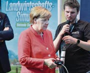 Bundeskanzlerin Angela Merkel lässt sich von Martin Rabl von Giants Software das Videospiel «Landwirtschaftssimulator» auf der Playstation 4 erklären. (Bild: Martin Meissner/Keystone (Köln, 22. August 2017))