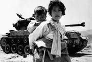 Mit ihrem Bruder auf dem Rücken stapft eine koreanische Jugendliche an einem Panzer der US-Armee vorbei. (Bild: R.V. Spencer/Keystone (Haengju, 9. Juni 1951))