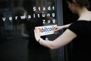 Eine Mitarbeiter der Zuger Stadtverwaltung bringt ein Bitcoin-Kleber am Eingang an. (Bild: Stefan Kaiser (Zug, 1. Juli 2016))