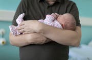 Ein Vater hält sein neugeborenes Kind in den Armen. (Bild: Gaetan Bally/Keystone)