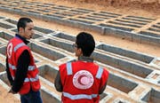 Zwei Mitarbeiter des Roten Halbmondes stehen beim Friedhof Bir el-Osta Milad in der Nähe der libyschen Hauptstadt Tripolis. (Bild: AFP/Mahmud Turkia)