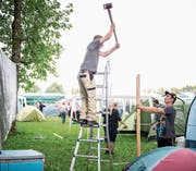 Es geht zur Sache auf dem Heitere: Christoph Bühler (links) hämmert mit Silvan Dober eine Holzstange in den Boden. Währenddessen werden weitere Utensilien auf das Gelände gekarrt (oben rechts) und das «böse Zäut» aufgebaut. (Bild: Roger Grütter (Zofingen, 8. August 2017))
