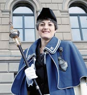Die derzeitige Standesweibelin Pascale Schriber hält den Weibelstab in der rechten Hand. Zum Weibelgewand gehört auch noch ein von einem Löwen getragenes Zuger Wappenschild. Der Erzengel Michael (Bild rechts) kämpft mit dem Drachen.
