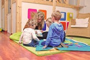 Szene in der Kindebetreuung: Eine Mitarbeiterin zeigt drei Schützlingen ein altersgerechtes Buch über den Stassenverkehr. (Bild: PD/Small Foot AG)