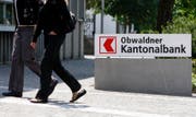 Zwei Personen vor einem Logo der Obwaldner Kantonalbank. (Symbolbild Keystone / Urs Flüeler)