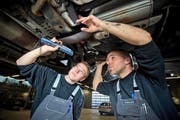Mechatroniker-Lehrling Markus Häfliger (links) und Automechaniker Marcel Isenschmid kontrollieren in einer Werkstatt in Oberkirch einen Autoauspuff. (Bild: Dominik Wunderli/Neue LZ)