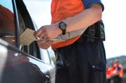 Ein Polizist kontrolliert Fahrzeugpapiere und Fahrausweis eines Autofahrers. (Bild: Keystone)