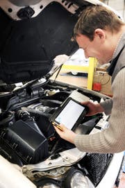 Ein Experte (mit Tablet in der Hand) blickt in der Prüfhalle des VSZ in Stans unter eine Motorhaube. (Bild Corinne Glanzmann)