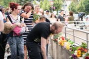 Eine Frau weint, während ein Mann beim Tatort Blumen niederlegt. (Bild: AP/Sebastian Widmann)