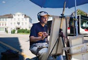 Unter dem Sonnenschirm und mit Kopfhörern malt Felix de la Concha derzeit rund um den Bahnhofplatz, wann immer es sonnig ist. (Bild: Coralie Wenger)