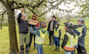 Mathis Müller (links) und Pascal Keller von der Vogelwarte Sempach helfen, die von den Muoler Viert- und Fünftklässlern selbst gemachten Nistkasten aufzuhängen. Interessiert beobachtet von Gemeindepräsident Bernhard Keller (Mitte) und Lehrerin Martina Keller. (Bild: Hanspeter Schiess)
