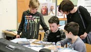 Drei Primarschüler beobachten, wie ihr programmierter, hellblau blinkender Roboter den schwarzen Linien auf dem Papier folgt. (Bild: Tim Frei)