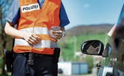 Ein Polizist überprüft bei einer Kontrolle die Fahrzeugpapiere und den Ausweis. (Bild: Christian Beutler/KEY)