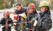Teamwork: Ein Kind pumpt, das andere löscht mit dem Strahlrohr einen kleinen Brand an einer Hausattrappe. Offizier Ivo Forster gibt Anweisungen. (Bild: Werner Lenzin)