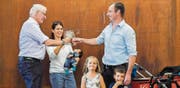 Der 4000. Gachnanger Anjo Gunsch bekommt auf dem Arm von Mami Natalie Gunsch wenig mit vom Trubel. Gemeindepräsident Matthias Müller stösst gleichwohl mit der stolzen Mama und Papi Christof Pfister an. Anjos ältere Geschwister Lena und Matteo finden's auch lässig. (Bild: Reto Martin)