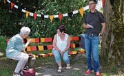 Anwohnerin Olga Häberli und Dorfkönigin Regula I. sitzen auf dem Bänkli, daneben steht Gemeinderat Peter Meier. (Bild: Christoph Heer)