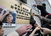 Demonstranten bringen nach dem ersten Verschwinden des Verlegers Gui Minhai 2016 dessen Porträt am Gebäude der chinesischen Regierung in Hongkong an. (Bild: Vincent Yu/AP (3. Januar 2016))