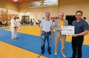 Ortsgemeindepräsident Rolf Heinzmann (Mitte) und Verwaltungsrat Koni Metzger übergeben den Check an Marcel Muttner vom Judoclub Tadashi Goldach. Links im Judogi steht Otto Fend (6. Dan), der das Training anlässlich des Einweihungsfestes in der Bachfeld-Turnhalle leitete. (Bild: jct)