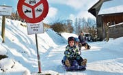 Felix und Melina sausen in ihrem Schlitten die Haustrasse hinunter, auch Nachbarin Nicole Allemann freut sich über die Piste. (Bild: Mario Testa)