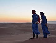 Zwei Berber in hellblauen Djellabas auf der höchsten Düne des Erg Chegaga – der Transatlas rechts am Horizont begrenzt das Sandmeer. (Bild: Mario Testa)