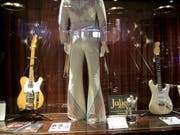 Auch sie wurden versteigert: Ein Bühnenkostüm von Pop-Sänger Elton John (m) und eine Gitarre (l), die Bob Dylan in einer entscheidenden Phase seiner Musik-Karriere begleitete. (Bild: Keystone/AP/MARK LENNIHAN)