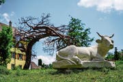 Die zwei Tonnen schwere Kuh von Steinmetz-Weltmeister Tobias Kupferschmidt liegt im Gras des Rotfarbareals, hinter ihr der Baum aus Metall von Thomas Urben. (Bild: Maya Heizmann)