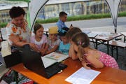 Daniela Gröbli, Autorin des Goldi Büchleins, schart zahlreiche Kinder um sich, die ihr beim Erzählen aufmerksam zuhören. (Bild: Rosmarie Berlinger, Buochs, 14. Juli 2018)