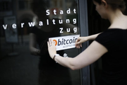 Eine Mitarbeiterin der Zuger Stadtverwaltung bringt einen Bitcoin-Kleber an. Die Stadt äussert sich nun zu einem potenziellen Reputationsrisiko. (Bild: Stefan Kaiser (Zug, 1. Juli 2016))