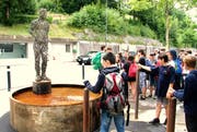 Auf einem Sockel im Brunnen steht eine lebensgrosse Figur aus rostigem Stahl.