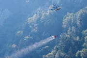 Ein Helikopter transportiert Löschwasser, um den Brandherd nach einem Kleinflugzeugabsturz am Lopper in Hergiswil im Kanton Nidwalden zu löschen. (Bild: Keystone/Urs Flüeler)